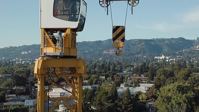 Tower crane with hills, houses, and elevated commuter train in background, Drone shot descending from crane cab.