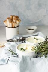 Cauliflower cream soup garnish with fresh cauliflower, thyme and bread in a white ceramic bowl. Autumn or winter comfort food. 