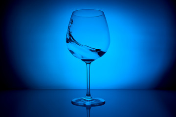wine glass with water splash on the lighting blue background