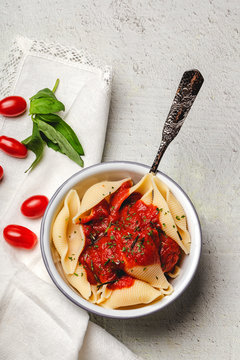 From above delicious conchiglie pasta sprinkled with basil and red tomatoes served on white plates and spoon