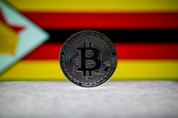 Physical silver version of Bitcoin (BTC) and Zimbabwe Flag on the background. Conceptual image for investors in cryptocurrency and Blockchain Technology.