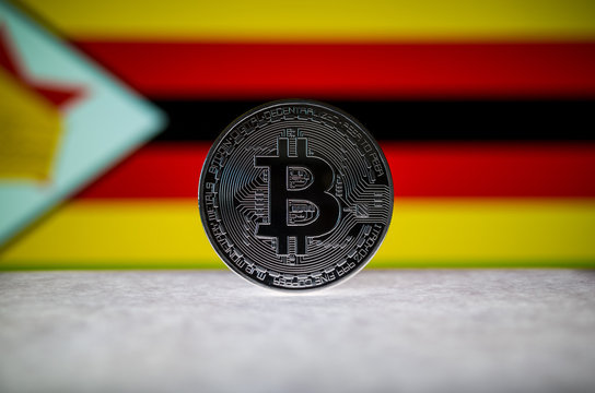 Physical silver version of Bitcoin (BTC) and Zimbabwe Flag on the background. Conceptual image for investors in cryptocurrency and Blockchain Technology.