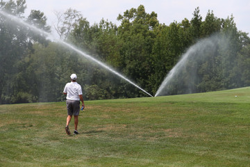 Golfers play as sprinkler systems water the golf course.