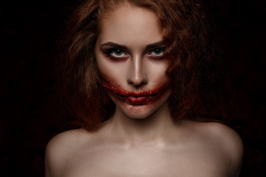 Ginger scary girl with cutted mouth looking her blue eyes to the camera. Halloween makeup