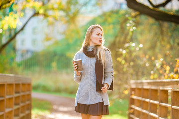 Fall concept - beautiful woman drinking coffee in autumn park under fall foliage