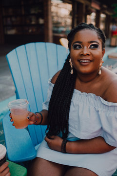 From above side view cheerful black african young woman drinking cold beverage while sitting at hipster cafe looking away