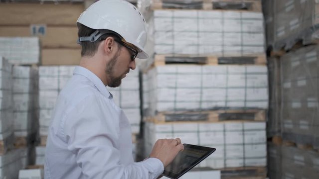 Worker male warehouse worker engineer man in a helmet working on the construction site of the warehouse, tablet computer, checking the warehouse, inspection of goods