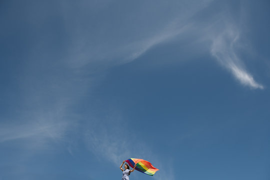 Side view of adult confident woman in casual dress carrying rainbow colored flag above head on windy day