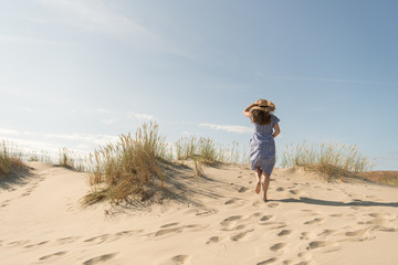 adult woman in casual dress and straw hat walking having good time on sand dune on hot summer day