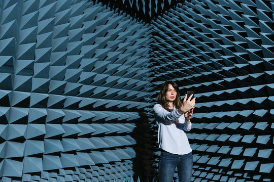 Modern brunette in casual outfit standing in contemporary sound room and taking selfie on phone