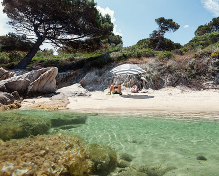 Tanned man enjoying rest under parasol in splendid place with crystal water and sandy beach in summer day, Halkidiki, Greece
