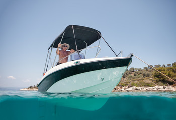 From below elderly man in hat and sunglasses sailing on black and white boat in calm turquoise water of Halkidiki, Greece
