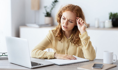 Bored woman with laptop and paperwork making notes