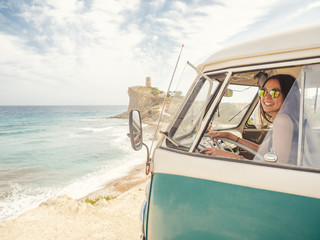 Side view of car with woman drawing on sandy empty beach with foamy waves in bright sunny day