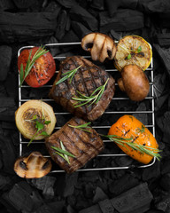Grid with prepared meat steak and vegetables on grill