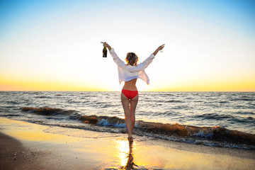 Young girl on the sea beach with a bottle of champagne and a glass