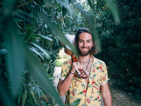Pensive bearded hipster man walking in jungle with ukulele looking at camera
