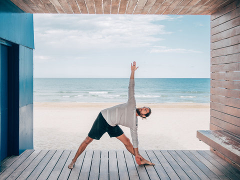 Adult fit bearded male doing yoga on wooden pier by seashore looking away - Powered by Adobe