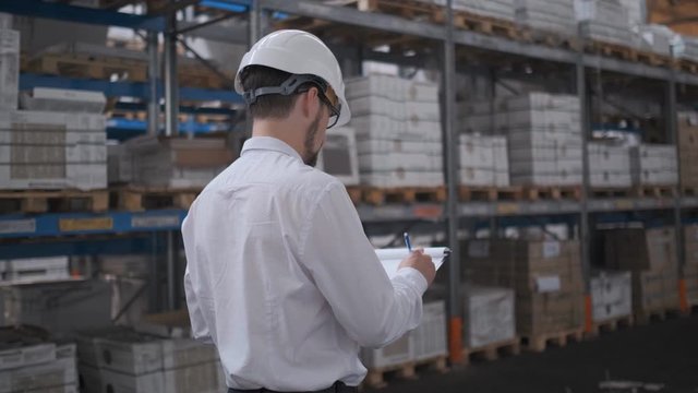 Employee male warehouse worker engineer man in hard hat working at construction site warehouse, walking in logistics center factory, engineer using tablet computer, architect businessman man indoors