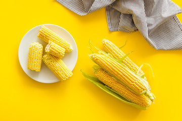 Cob corns and fresh corn on plate on yellow background top view