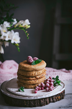 Stack of raspberry pancakes with fresh berry on porcelain plate at marble tabletop text to case with flowers over dark background