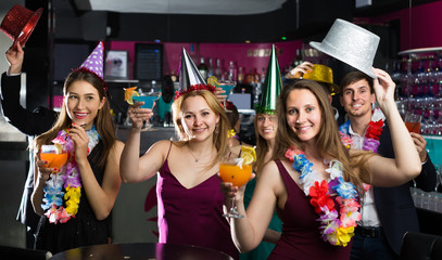 Fototapeta premium Portrait of young positive women and men in caps with cocktails