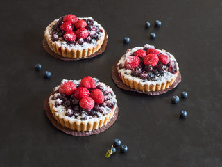 Beautiful delicious tarts, colorful pastry cakes sweets with fresh raspberries and blueberry on black background