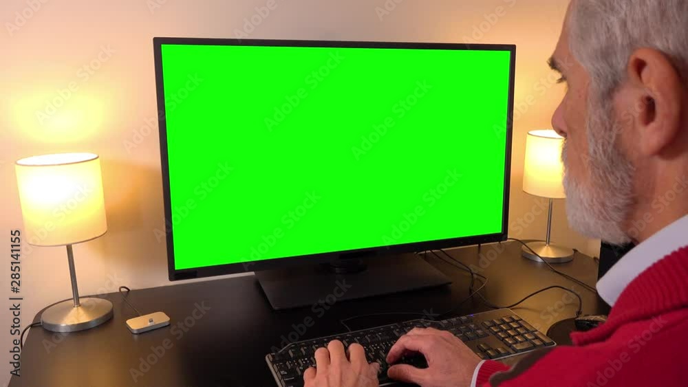 Wall mural an elderly man works on a computer with a green screen in an apartment - closeup - types on keyboard