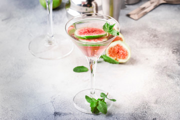 Pink fig martini cocktail in shot glass on gray table with bar tools, selective focus