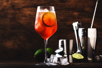 Campari tonic alcoholic cocktail with red bitter, tonic, lime and ice. Old wooden table background, bar tools, selective focus. All names refer to cocktails, not trademarks