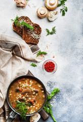 Autumn or winter meat vegetable mushroom hot soup with beef and wholegrain barley. With black breaв and parsley, top view, gray kitchen table, copy space