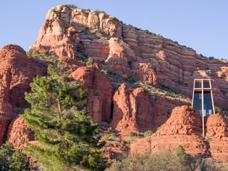 Red rock massif with Chapel of the Holy Cross near Sedona seen in a bright spring sunny afternoon with a large pine tree in foreground