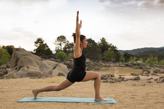 Young woman doing yoga poses outdoors on a cloudy day next to a dam beach