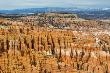 Central part of Bryce canyon (Bryce amphitheater) in spring. Some snow still remains on the tops of colorful cliffs and pinnacles. Mountains in distance