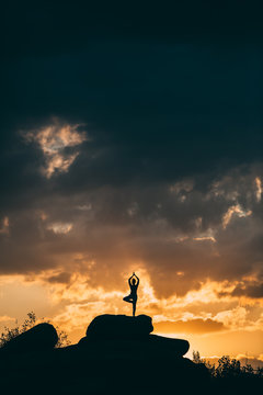 silhouette of woman doing yoga poses outdoors on a amazing sunset while standing on rock