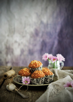 Plate with tasty grain muffins placed near linen napkin and pink flowers on wooden tabletop