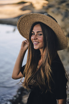 Young long haired smiling female model looking away holding hat in air on beach