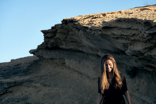 Young long haired stylish pensive female model looking down standing in sunlight with hills on background