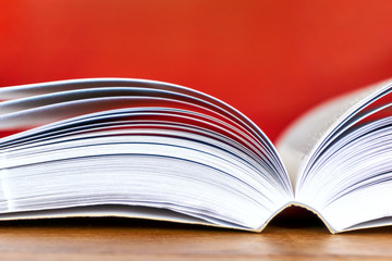 Open text book with visible pages on wooden desk against a red background. Back to school, education or study concept. Closeup side view shot with selective focus. and copy space