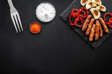Obraz na płótnie Canvas Grilled sausages, vegetables on kitchen board and spices on black background top view mock-up