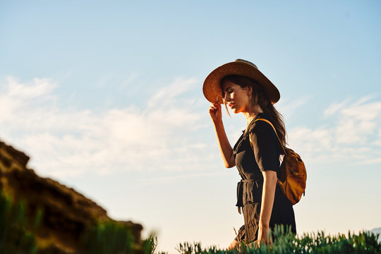 Side view of female tourist wearing a straw hat and backpack walking