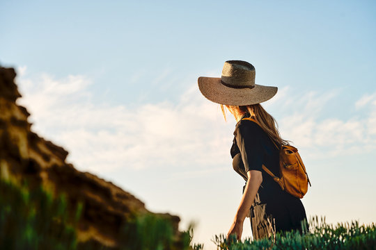 Side view of female tourist wearing a straw hat and backpack walking
