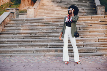 Fashionable girl in a summer city. Black lady in a green jacket. Woman in a red scarf. Famale with sunglasses