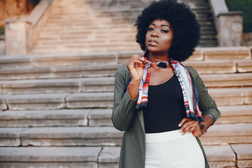 Fashionable girl in a summer city. Black lady in a green jacket. Woman in a red scarf. Famale with sunglasses