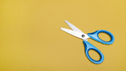 Opened blue scissors over yellow background. 