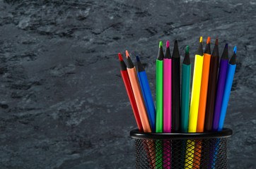 Pencil tray on a black background with colored pencils. Copy space.