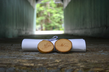 Rustic Mr. & Mrs. signs cut from tree branches sit in front of a rolled marriage license at the end of a covered wooden bridge