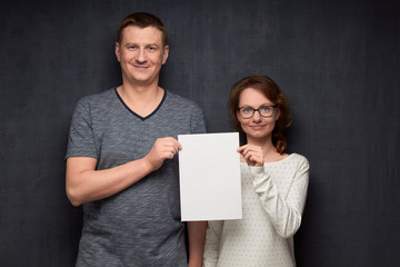 Portrait of couple holding white blank paper sheet together