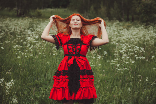 pretty redheaded woman in Little Red fairytale dress in the grass meadow