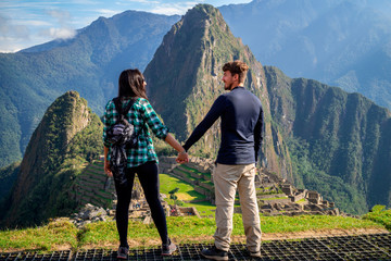 Young couple holding hands looking each other in a terrace of Machu Picchu. One of the Seven...